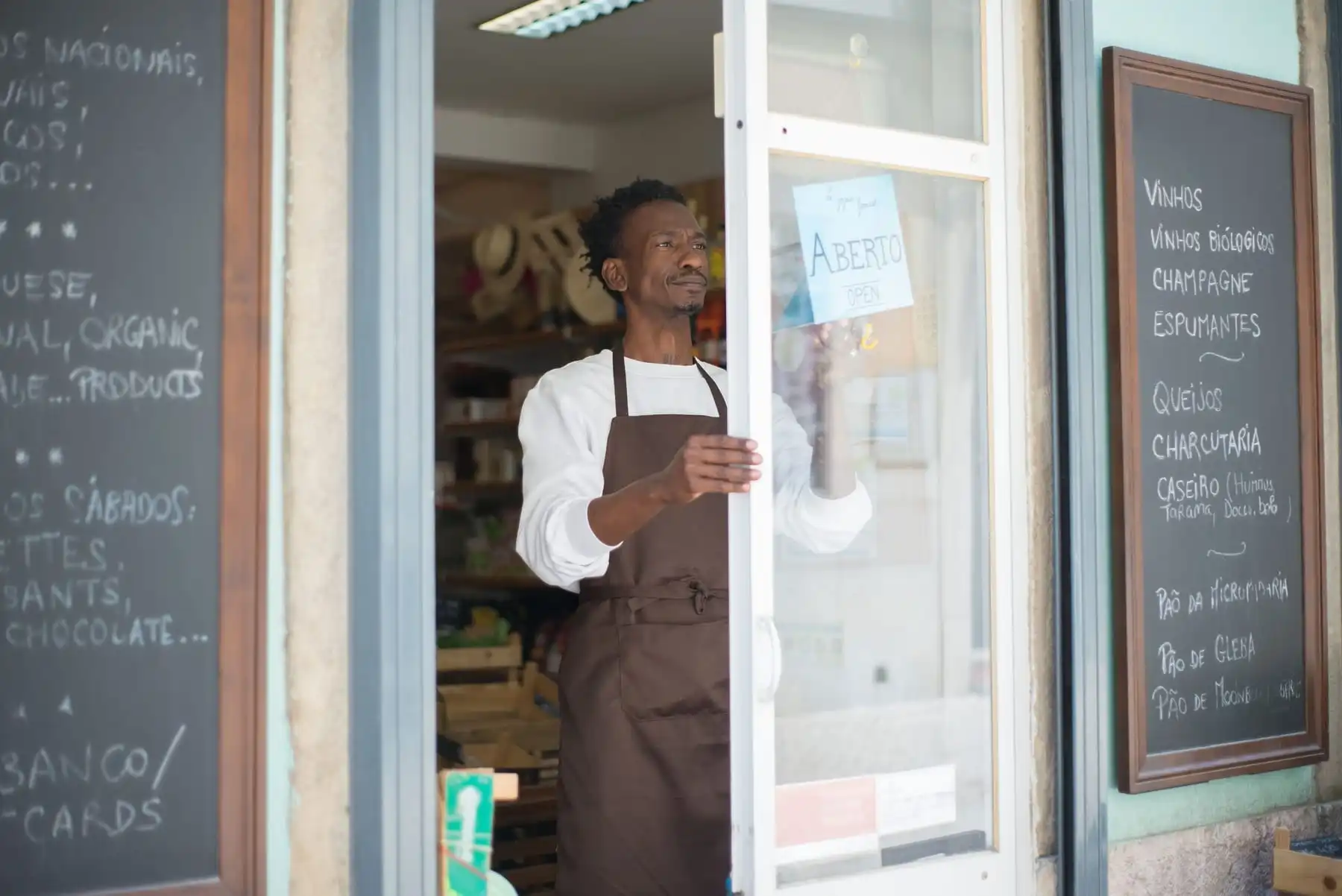 A grocer in an apron opening the glass door of his shop in the morning