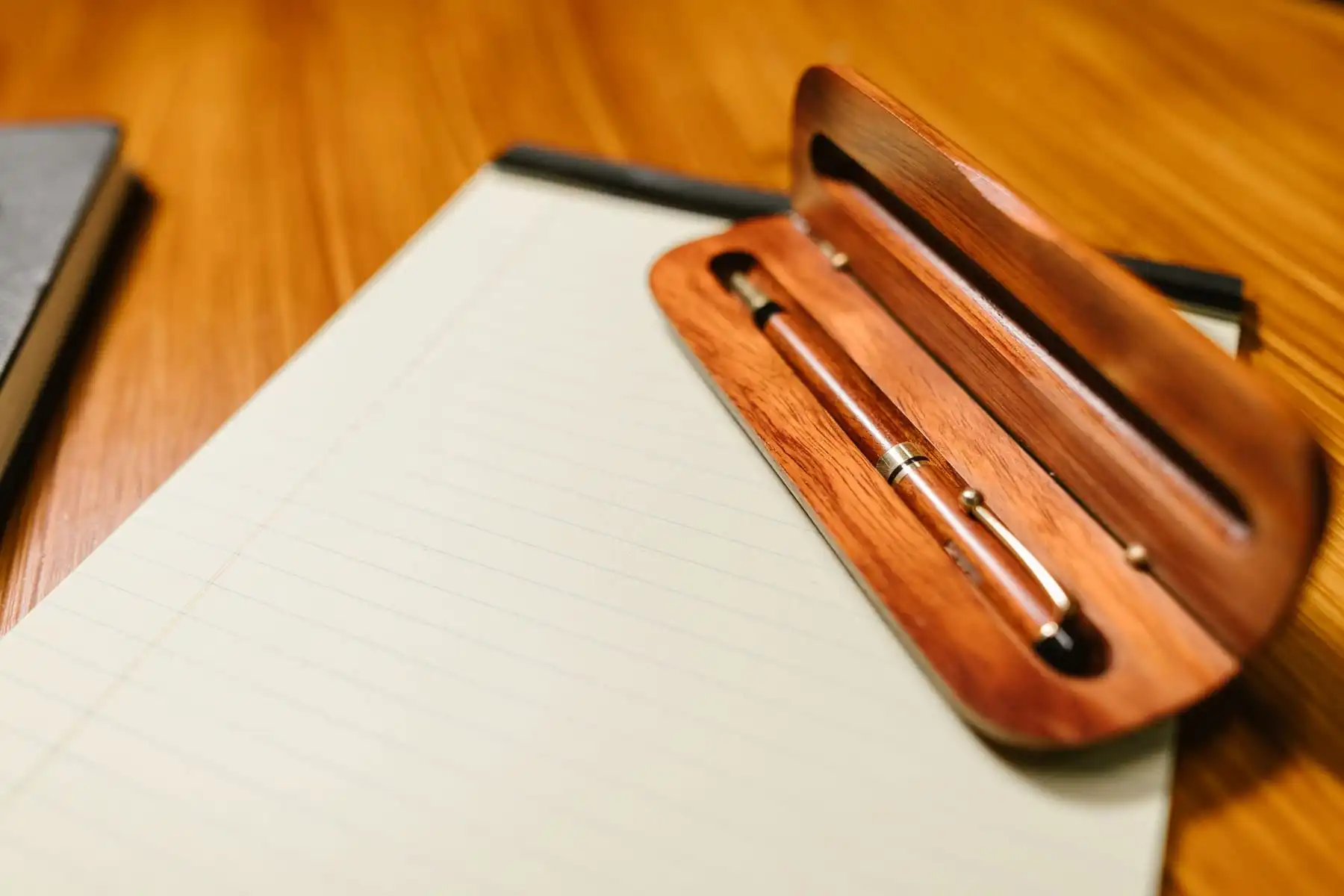 A wooden pen resting on a lined notepad on a warm wooden desk
