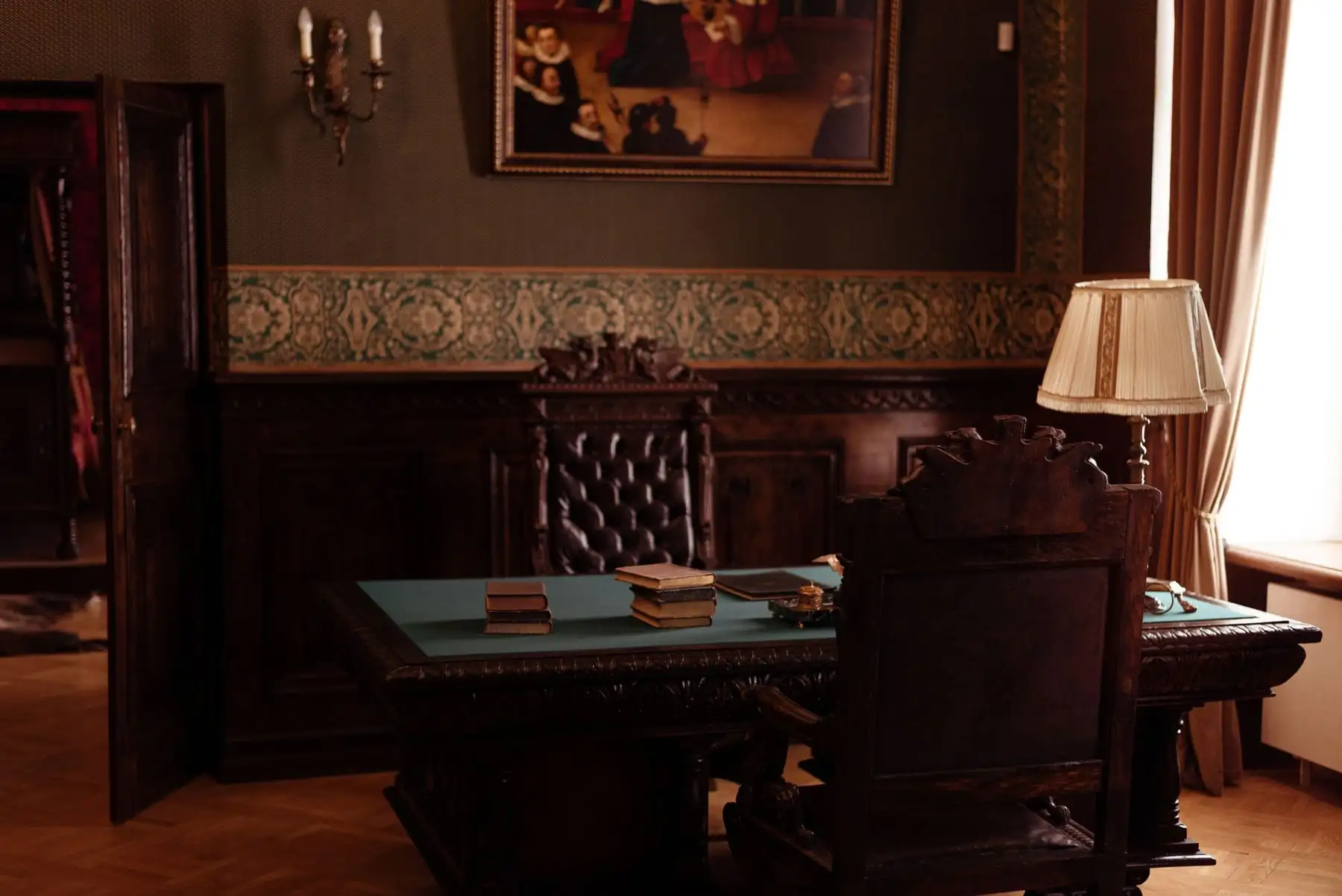 A quiet wood-panelled study with a leather chair at the desk and a lamp lit beside the window